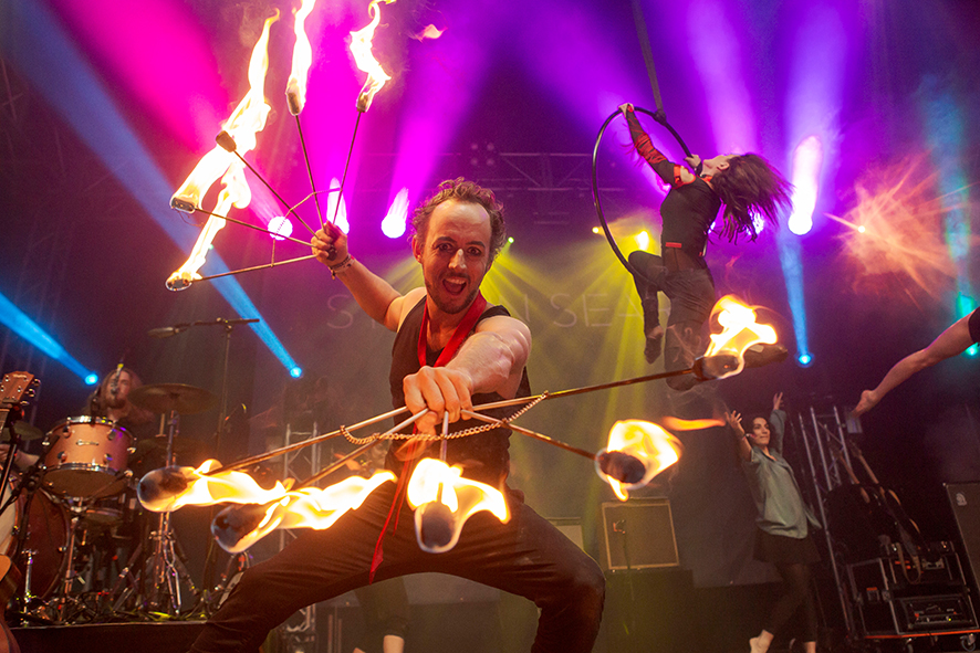 Mann mit brennenden Fchern, einer Band und Frau im hngenden Aerial Hoop. (/images/bilder/thumbs/715_2_bild_Feuershow-Konzert.JPG)